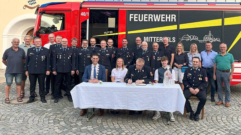 Die Marktgemeinde Mitterfels ehrt den neuen KBR Markus Weber (sitzend, Mitte) mit Gattin Daniela und Sohn Patrick mit seinem bereits zweiten Eintrag ins Goldene Buch. Bürgermeister Andreas Liebl (sitzend, links), FFW-Vorsitzender Kilian Graf (sitzend, rechts), und weitere Gäste aus der Feuerwehr und dem Marktgemeinderat begleiteten die Zeremonie und auch das neue HLF 20 (Hilfeleistungslöschgruppenfahrzeug) durfte mit ins Bild. Die Marktgemeinde Mitterfels ehrt den neuen KBR Markus Weber (sitzend, Mitte) mit Gattin Daniela und Sohn Patrick mit seinem bereits zweiten Eintrag ins Goldene Buch. Bürgermeister Andreas Liebl (sitzend, links), FFW-Vorsitzender Kilian Graf (sitzend, rechts), und weitere Gäste aus der Feuerwehr und dem Marktgemeinderat begleiteten die Zeremonie und auch das neue HLF 20 (Hilfeleistungslöschgruppenfahrzeug) durfte mit ins Bild.