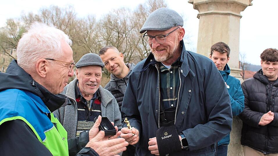 Wolfgang Bogie (links) &uuml;berreichte die Ehrung an Christian Berger von der Fahrradwerkstatt im Ankerzentrum auf der Steinernen Br&uuml;cke vor dem 'echten' Bruckmandl.