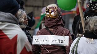 Eine Frau tr&auml;gt eine Maske auf dem Hinterkopf und ein Plakat mit der Aufschrift 'Maske = Folter' bei einer Demonstration von mehreren tausend Menschen gegen Corona-Ma&szlig;nahmen und Impfpflicht im Februar in Frankfurt.