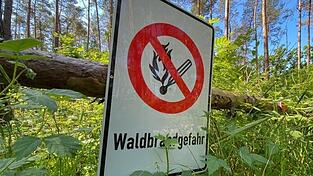 Ein Schild mit der Aufschrift 'Waldbrandgefahr' hängt an einem Baumstamm.