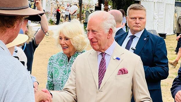Da sind sie: K&ouml;nig Charles und K&ouml;nigin Camilla gehen mit freundlichem L&auml;cheln die Reihe der Wartenden ab.