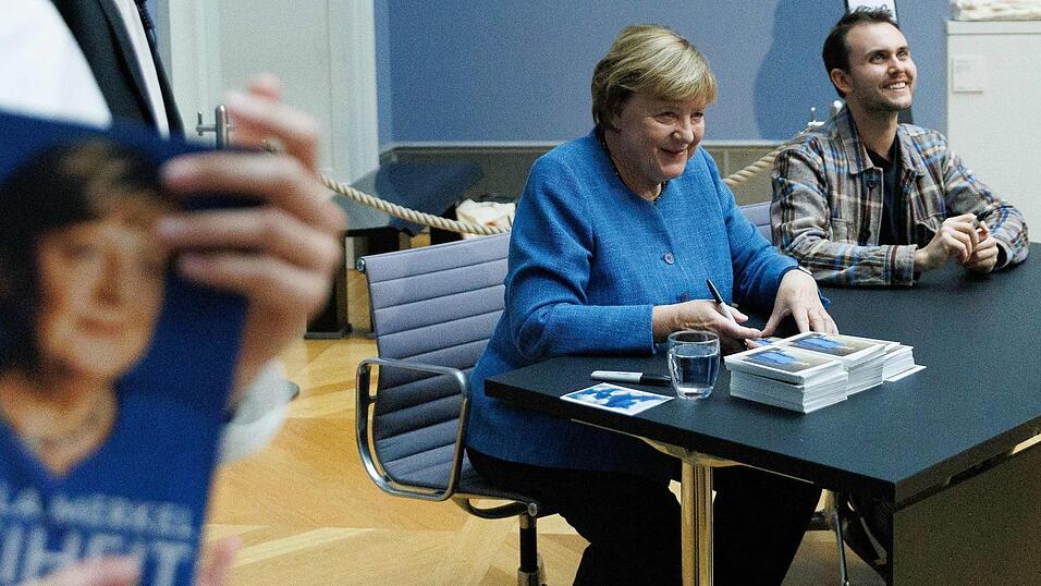 Merkel signiert Kunstpostkarten im Bode-Museum neben dem Maler ihres dort ausgestellten Portr&auml;ts, J&eacute;r&eacute;mie Queyras.
