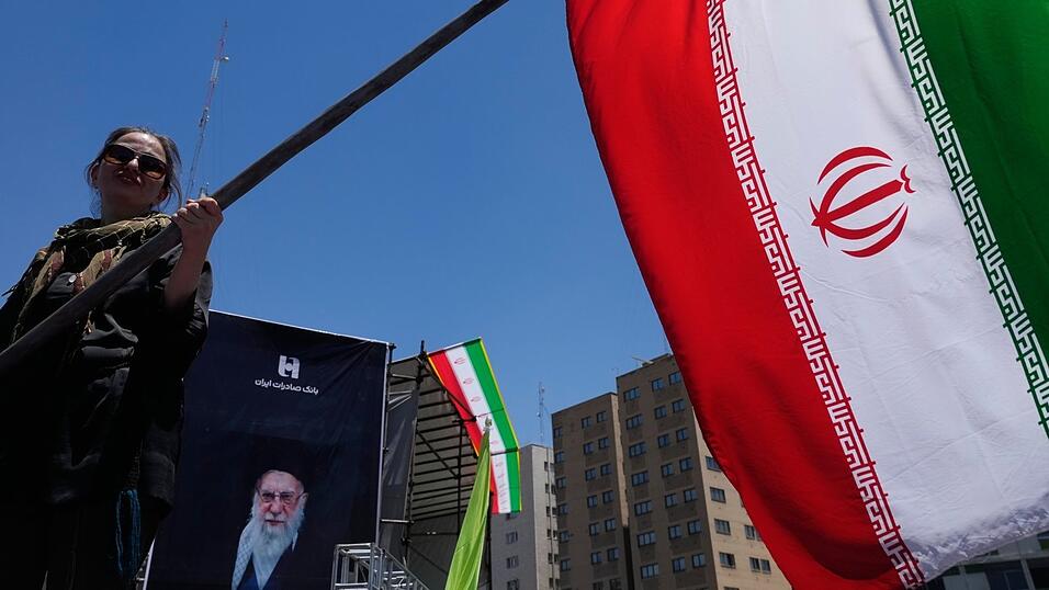 Eine Frau schwenkt während einer regierungsfreundlichen Kundgebung eine iranische Flagge, während im Hintergrund ein Porträt des ermordeten Obersten Führers Führer Ajatollah Ali Chamene zu sehen ist. Eine Frau schwenkt während einer regierungsfreundlichen Kundgebung eine iranische Flagge, während im Hintergrund ein Porträt des ermordeten Obersten Führers Führer Ajatollah Ali Chamene zu sehen ist.