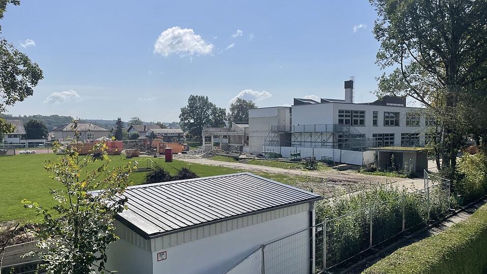 Mehrere Container, ein Bagger und ein knallrotes Dixiklo stehen auf dem Sportplatz. Von der Turnhalle sind noch einzelne Betonträger zu sehen.