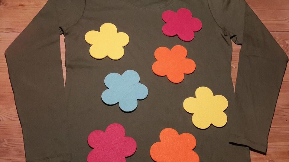 Blumenwiese: Wer die Blumenwiese perfekt machen will, kann im Handumdrehen zum Blumenhut noch das passende Oberteil gestalten: Einfach auf ein gr&uuml;nes Shirt auf Vorder- und R&uuml;ckseite Blumen mit doppelseitigem Klebeband befestigen. Die Blumen kann man zum Beispiel aus Tonpapier oder aus Filz ausschneiden. Wer mag, kann noch Schmetterlinge oder andere Wiesenbewohner aufkleben.