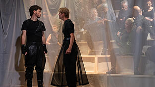 Macbeth (Aaron Jungblut-Klemm) und seine Lady (Gabi Butz) am R&auml;nkeschmieden w&auml;hrend eines Festgelages im Hintergrund