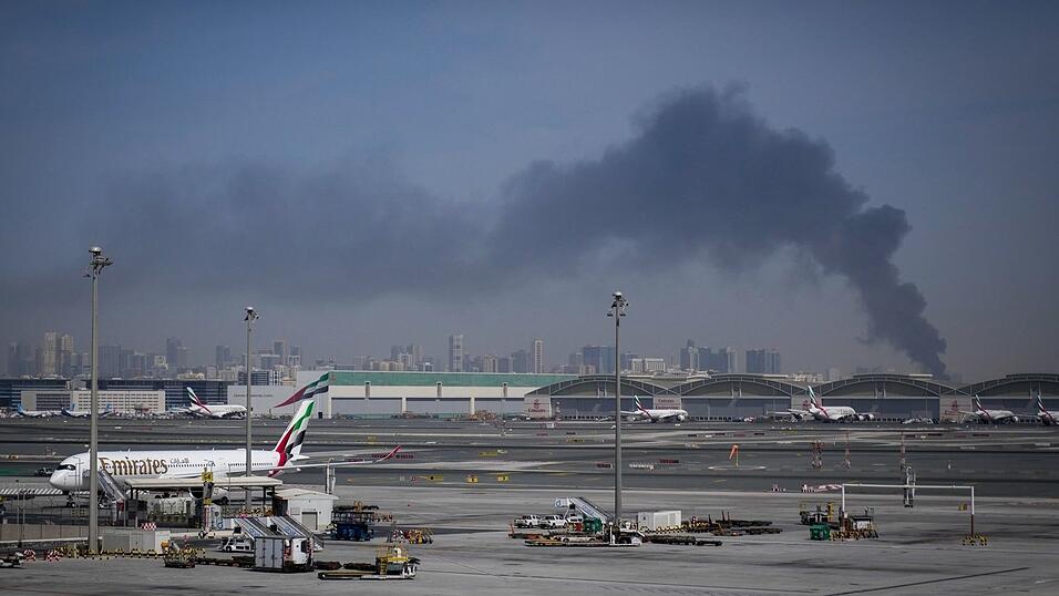 Eine Rauchwolke im Hintergrund, w&auml;hrend Flugzeuge auf dem geschlossenen Dubai International Airport geparkt sind.