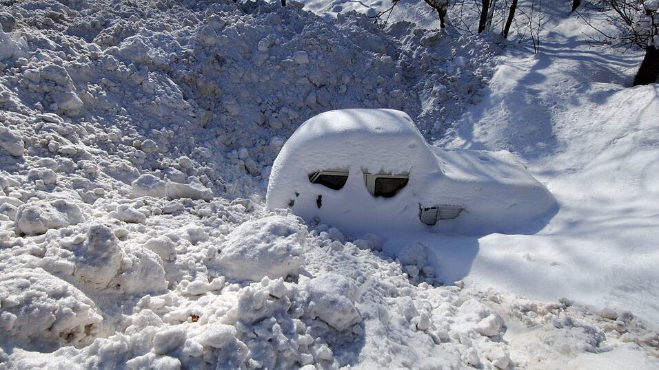 Ein Auto - eingeschneit und umschlossen von Schneemassen - auf einem Parkplatz. (Archivbild)