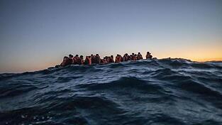 Migranten aus verschiedenen afrikanischen Nationen warten in einem Boot vor der libyschen Küste im Mittelmeer auf Helfer.