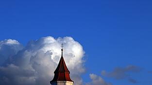 Wolken türmen sich hinter einem Kirchturm.