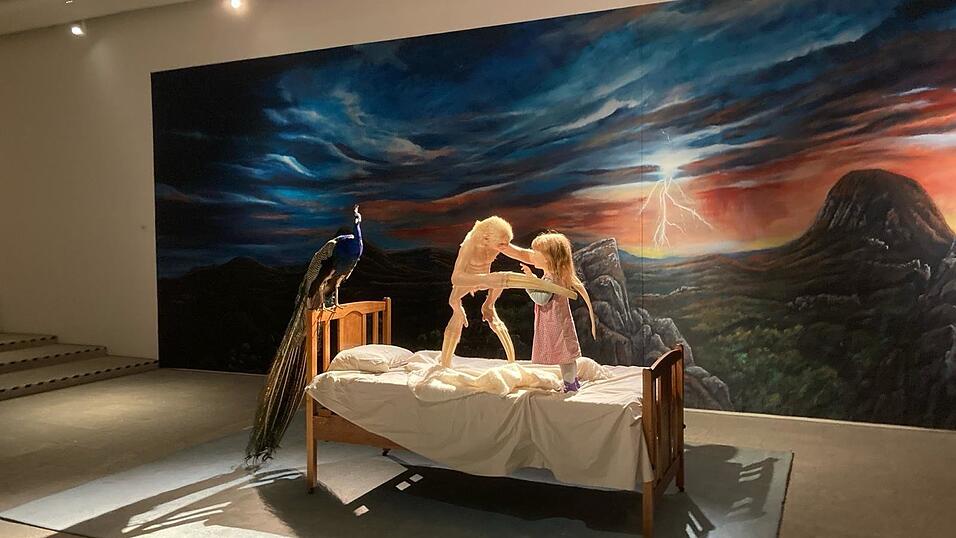 Eine Begegnung der - vermeintlich - unheimlichen Art vor schauriger Kulisse mit Pfau: Diese Installation von Patricia Piccinini hat denselben Titel wie die Ausstellung &bdquo;The welcome Guest&ldquo;.