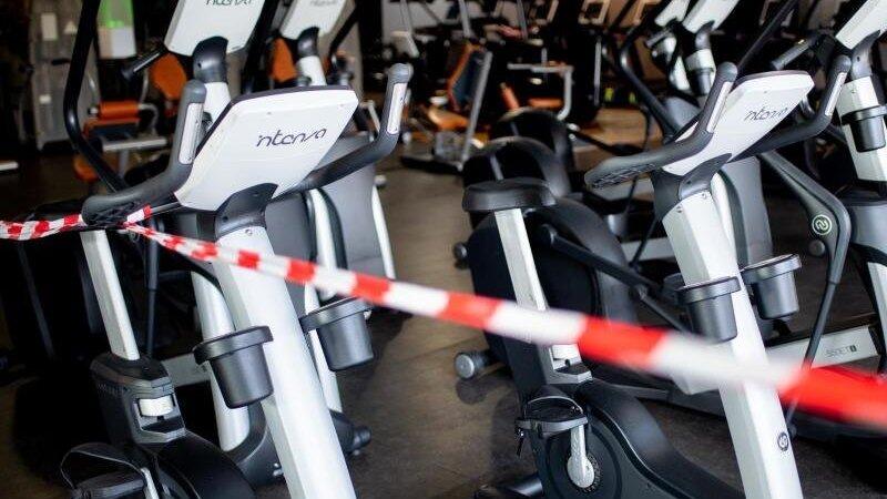 Ein rot-weißes Flatterband ist an Fahrradtrainern befestigt, die in einem Fitnessstudio stehen. Foto: Hauke-Christian Dittrich/dpa/Archivbild