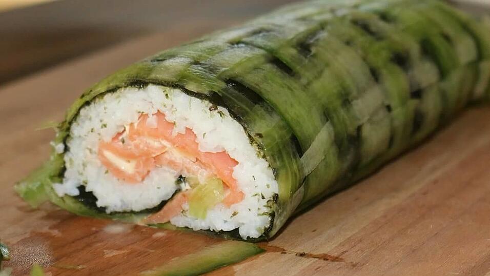 Sushi in einer Vorstufe der Zubereitung. Die feinen Reisröllchen aus Japan sind hier noch als große Sushi-Rolle erkennbar. Als nächster Schritt wird die Rolle in dünne Scheiben geschnitten.