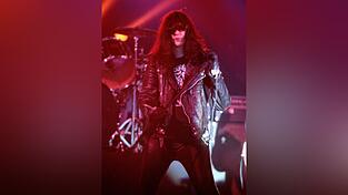 Ein Foto zeigt Sänger Joey Ramone auf der Neumarkter Bühne stilecht mit schwarzer Lederjacke, dunkler Sonnenbrille und Wischmopp-Frisur.