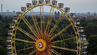Das Riesenrad des temporären Freizeitparks 'NürnBärLand' erhebt sich vor der Stadtkulisse in der Abendsonne.