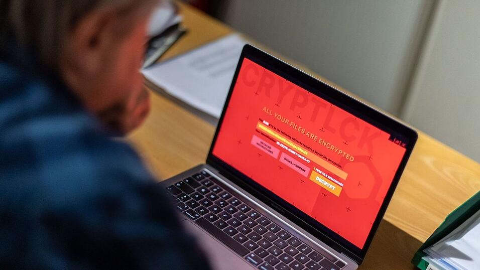 Ein Mann sitzt in einem Büro vor einem Laptop, der mit einem fiktiven Verschlüsselungstrojaner (Ransomware) befallen ist. Ein Mann sitzt in einem Büro vor einem Laptop, der mit einem fiktiven Verschlüsselungstrojaner (Ransomware) befallen ist.