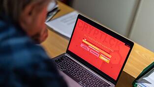 Ein Mann sitzt in einem Büro vor einem Laptop, der mit einem fiktiven Verschlüsselungstrojaner (Ransomware) befallen ist. Ein Mann sitzt in einem Büro vor einem Laptop, der mit einem fiktiven Verschlüsselungstrojaner (Ransomware) befallen ist.