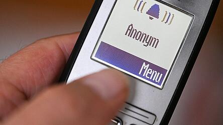 Eine Hand hält ein Festnetztelefon, auf dem ein anonymer Anrufer angezeigt wird. Eine Hand hält ein Festnetztelefon, auf dem ein anonymer Anrufer angezeigt wird.