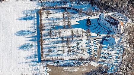 Der winterliche Friedhof aus der Luft mit den beiden Teilen von Kirche und Gemeinde und der Kirche St. Ulrich.