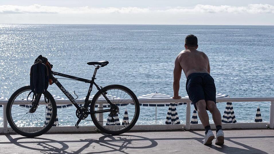 Ein Mann mit nacktem Oberkörper macht am Strand von Nizza neben seinem Fahrrad Übungen. (Archivbild)