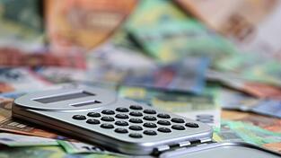 Ein Taschenrechner liegt auf verschiedenen Euro-Banknoten. (Symbolbild)