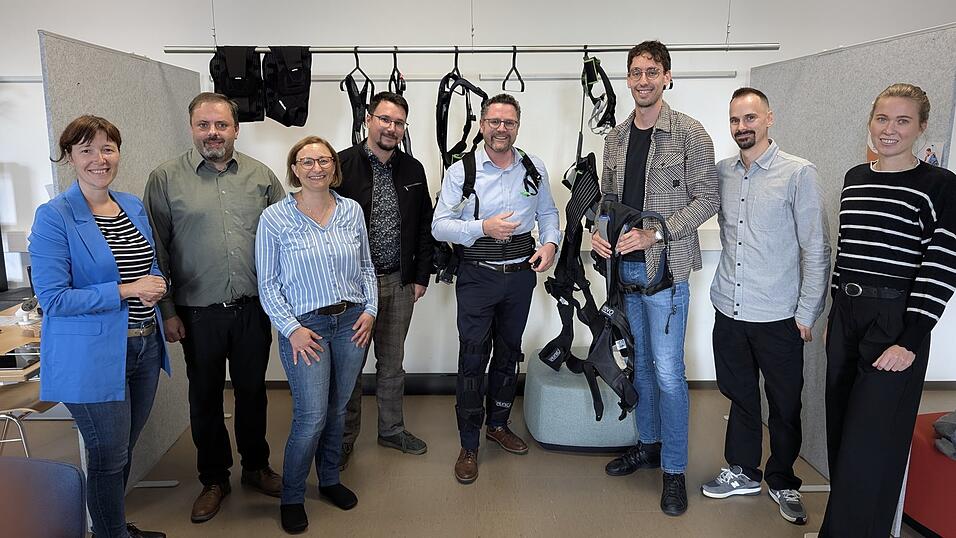MdL Dr. Gerhard Hopp (M.) lässt sich bei seinem Besuch von Lukas Schmidbauer das passive Exoskelett erklären - ganz links Kathrin Martin, operative Leitern des Gesundheitscampus.