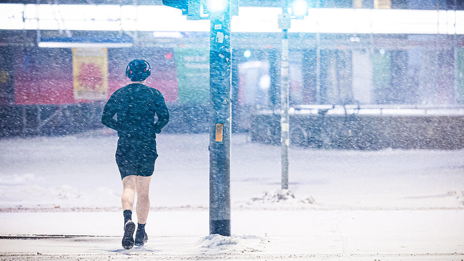 Ein Jogger l&auml;uft am fr&uuml;hen Morgen im dichten Schneefall.