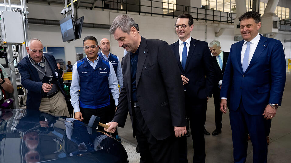 Markus S&ouml;der (CSU) bringt mit einem Hammer das BMW-Logo an einem Auto an. Hinter ihm stehen der k&uuml;nftige BMW-Chef Milan Nedeljkovi(&acute;c) (2. v. l.) und Werkleiter Robert Engelhorn (r.).