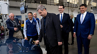 Markus S&ouml;der (CSU) bringt mit einem Hammer das BMW-Logo an einem Auto an. Hinter ihm stehen der k&uuml;nftige BMW-Chef Milan Nedeljkovi(&acute;c) (2. v. l.) und Werkleiter Robert Engelhorn (r.).