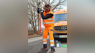 Der Fachmann sch&uuml;ttet das Kaltmischgut in die Schadstelle und presst es mit einem Handstampfer fest an, um die Fahrbahn wieder sicher zu machen.