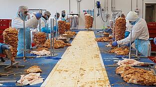 Über ein Förderband schicken die 'Stecker' die bis zu 65 Kilo schweren Dönerspieße zu den beiden Verpackern am Ende des Tisches. Die Marinade hinterlässt zwar ihre Spuren auf der Arbeitsfläche, in der Produktion gelten aber hohe Hygienestandards, betont Duygu Uguz. Einmal in der Woche kontrolliert das Veterinäramt die Dönerherstellung
