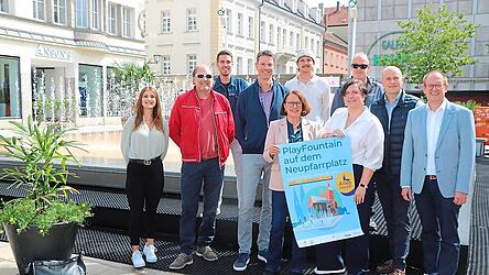 Oberbürgermeisterin Gertrud Maltz-Schwarzfischer und die Vorsitzende des Vereins Faszination Altstadt Maria Müller mit dem Play Fountain-Plakat. Mit im Bild sind Markus Bayer (Sparkasse, rechts), Robert Greb (Rewag, Vierter von links) und Ice-World-Geschäftsführer Robert Buchner (Zweiter von links).
