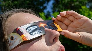Eine junge Frau schaut durch eine Sonnenfinsternisbrille und betrachtet die Mittagssonne. Eine junge Frau schaut durch eine Sonnenfinsternisbrille und betrachtet die Mittagssonne.