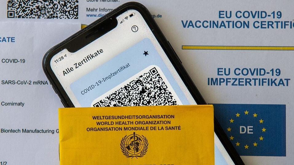 Ein Impfpass und ein Smartphone mit der CovPass-App liegen auf einem Impfzertifikat.