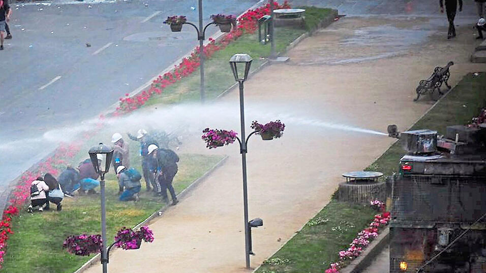 Über dem Plaza de Viña in Chile hängt eine Tränengaswolke, die Menschenmenge wirft Klopapierrollen in die Luft und schwenkt Chile-Flaggen.Die Proteste im Zentrum von Viña del Mar werden mit einem Wasserwerfer aufgelöst. Im Hintergrund eine Straßenblockade. Fotos: Bea Escherich Über dem Plaza de Viña in Chile hängt eine Tränengaswolke, die Menschenmenge wirft Klopapierrollen in die Luft und schwenkt Chile-Flaggen.Die Proteste im Zentrum von Viña del Mar werden mit einem Wasserwerfer aufgelöst. Im Hintergrund eine Straßenblockade. Fotos: Bea Escherich