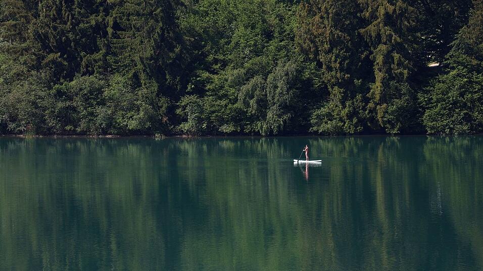 Eine Frau paddelt auf einem Stand-up-Paddle-Board über den Forggensee. Eine Frau paddelt auf einem Stand-up-Paddle-Board über den Forggensee.