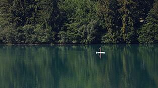 Eine Frau paddelt auf einem Stand-up-Paddle-Board &uuml;ber den Forggensee.