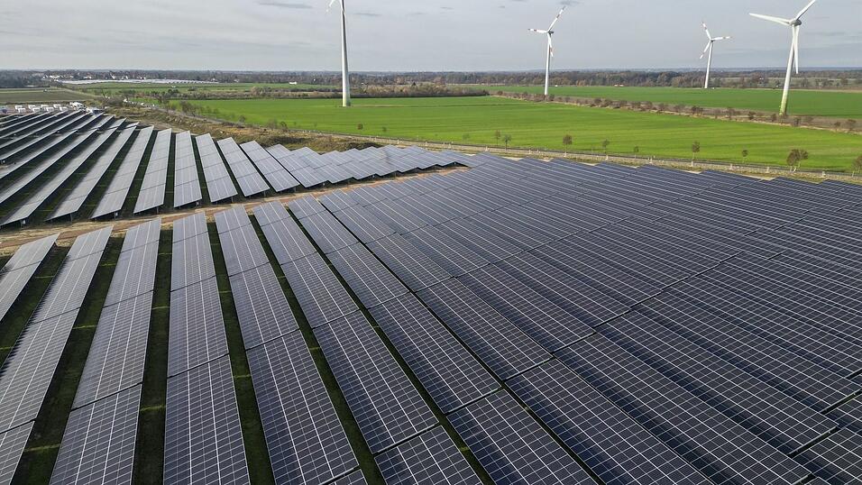 Windkraftanlagen drehen sich hinter Solaranlagen.