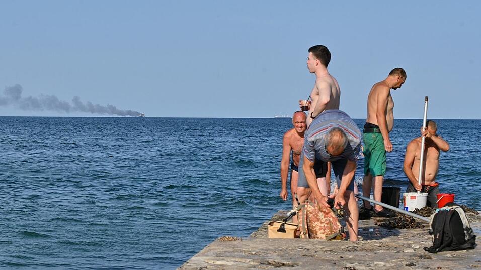 Menschen in Odessa sonnen sich, während am Horizont im Schwarzen Meer der brennende Getreidetransporter «Golden Leo» zu sehen ist. (Archivbild) Menschen in Odessa sonnen sich, während am Horizont im Schwarzen Meer der brennende Getreidetransporter «Golden Leo» zu sehen ist. (Archivbild)