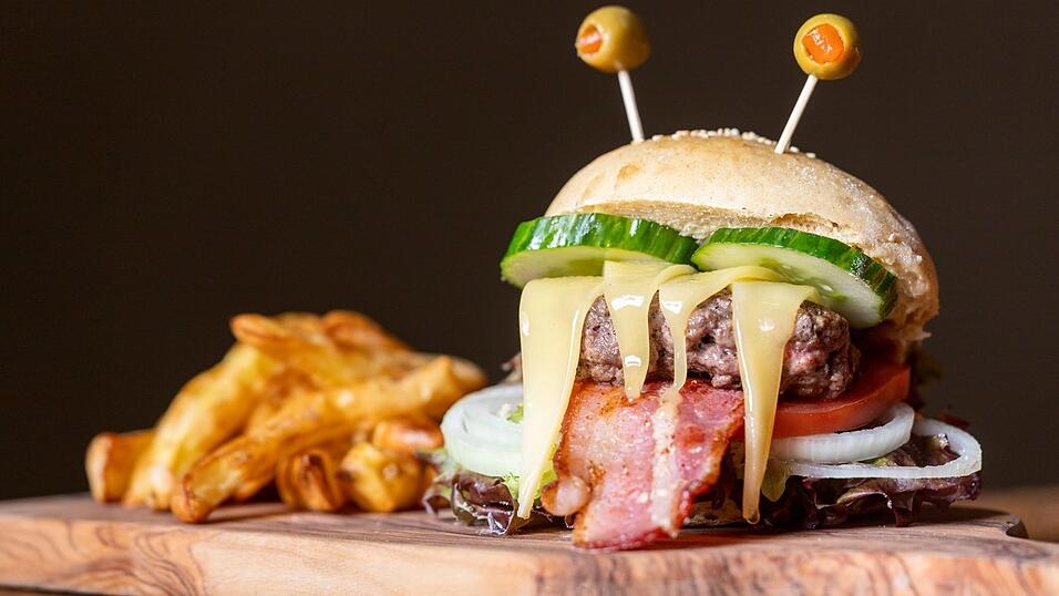 Ein Monster-Burger mit Olivenaugen macht hungrige Gäste satt. Beim Belag sind der Kreativität keine Grenzen gesetzt. Gurken, Bacon, Käse und Ketchup setzen das Monströse in Szene.