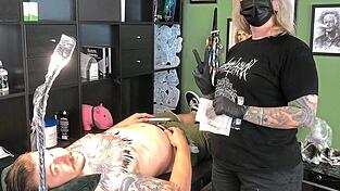 Oliver Wittman und Melanie Hankofer im 'Black Torch Tattoo Crew' in Deggendorf. Oliver l&auml;sst die blauen Pfeilspitzen seines Brusttattoos von der Kollegin schwarz &uuml;berstechen.