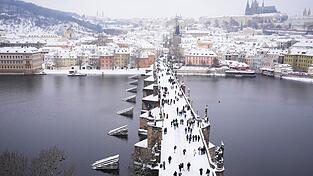 Menschen &uuml;berqueren die mittelalterliche Karlsbr&uuml;cke nach starkem Schneefall.