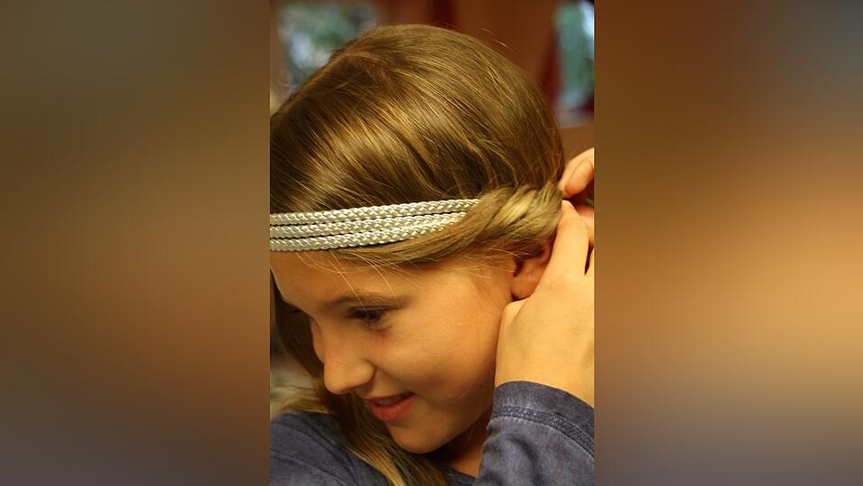 2. Dann nimmt sie von einer Seite eine Haarstr&auml;hne, legt sie locker um das Haarband und schiebt sie von oben nach unten in das Band. Dabei arbeitet sie von vorne bis zur Mitte des Hinterkopfes und beginnt dann von der anderen Seite. Haare, die noch wegstehen, fixiert sie mit Haarnadeln. Das Ganze sollte ruhig etwas locker und unordentlich aussehen, nicht so streng wie bei einem Dutt.