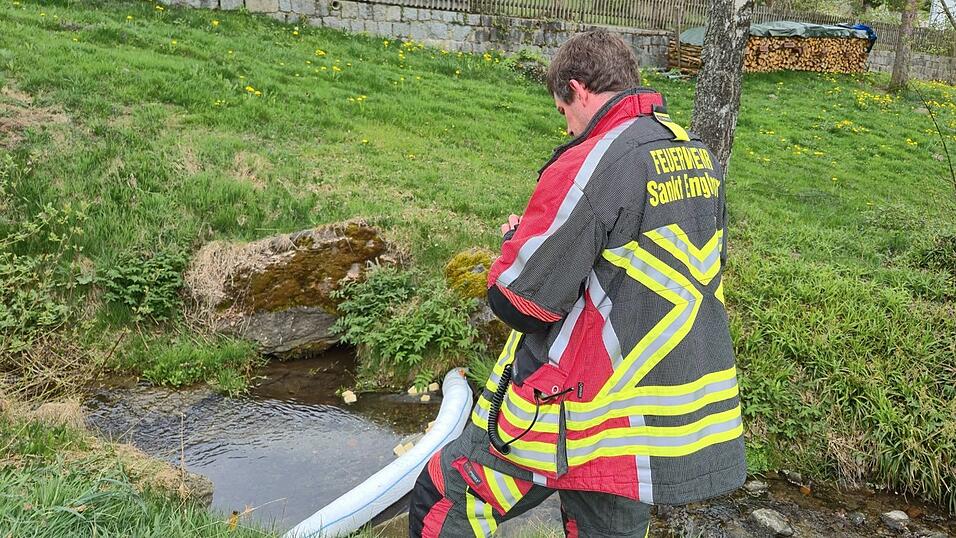 Ein Feuerwehrmann steht am Dorfbach neben der Ölsperre, die eine Ausbreitung der Verunreinigung verhindert.