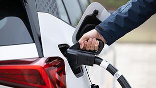 Ein Mann steckt ein Ladekabel in den Tankstutzen eines Elektroautos. Ein Mann steckt ein Ladekabel in den Tankstutzen eines Elektroautos.