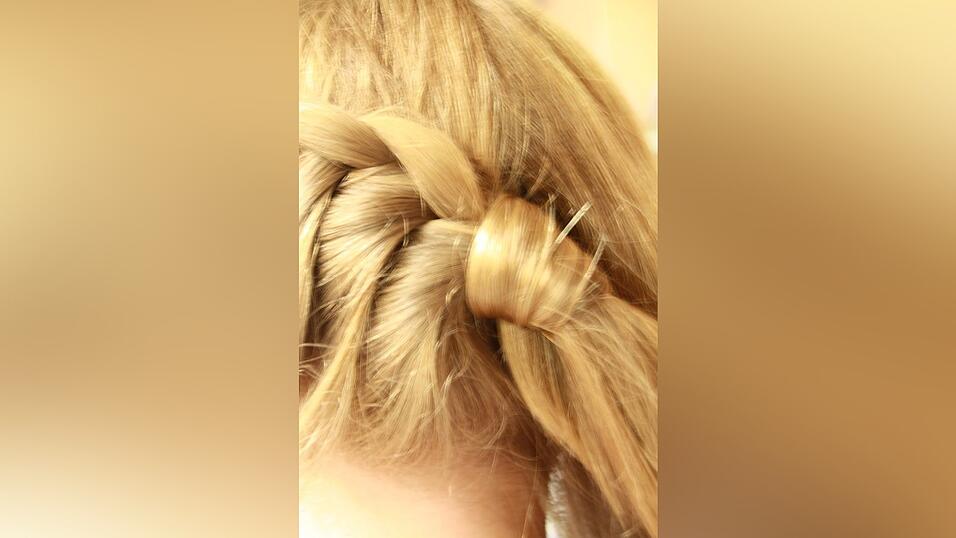 2. Den geflochtenen Zopf fixiert sie mit einem Gummi und umwickelt ihn mit einer Haarstr&auml;hne.