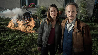 Frederike Bader (Marie Leuenberger) und Ferdinand Zankl (Michael Ostrowksi) vor einem brennenden Motorrad in einer Szene aus der Folge 'Der rote Wolf' aus der Krimireihe 'Ein Krimi aus Passau' (undatiert). Der Krimi 'Der rote Wolf. Ein Krimi aus Passau' wird am 11.09.2025 in der ARD ausgestrahlt. 