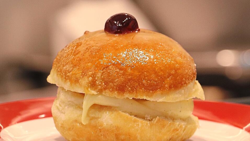 Eine kleine Kirsche thront auf diesem zuckerglasierten Vanillekrapfen.