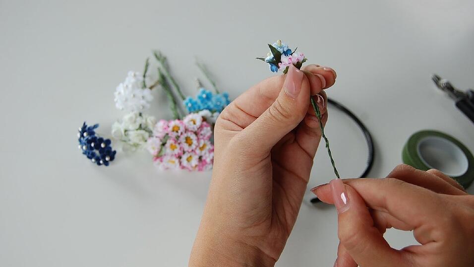 1. Den Haarreif brauchst du erst später. Erst werden die Blümchen aneinander gebunden. Und zwar zwei einzelne Hälften, die später am Reif befestigt werden. Am Ende soll es so aussehen, als würden die Blümchen an beiden Seiten nach oben 'wachsen'. Überlege dir vorher schon mal, wie in etwa du sie anordnen willst. Leg die ersten beiden Blüten der Länge nach übereinander, so dass die untere Blüte die andere überragt. Dann drehe die Drähte der beiden Blüten ineinander. 1. Den Haarreif brauchst du erst später. Erst werden die Blümchen aneinander gebunden. Und zwar zwei einzelne Hälften, die später am Reif befestigt werden. Am Ende soll es so aussehen, als würden die Blümchen an beiden Seiten nach oben 'wachsen'. Überlege dir vorher schon mal, wie in etwa du sie anordnen willst. Leg die ersten beiden Blüten der Länge nach übereinander, so dass die untere Blüte die andere überragt. Dann drehe die Drähte der beiden Blüten ineinander.
