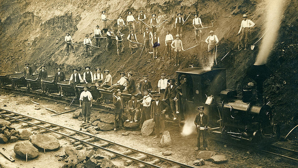 Der Bayerische Wald wurde sehr sp&auml;t durch die Eisenbahn erschlossen, was sich f&uuml;r die ersten Industrialisierungsans&auml;tze in der Region als hinderlich erwies. Erst 1877 wurde die Strecke Plattling &ndash; Bayerisch Eisenstein in Betrieb genommen. Die Ansichtskarte zeigt knapp 40 Arbeiter mit einer kleinen Behelfslok beim Bau des Streckenabschnitts Obernzell &ndash; Untergriesbach der Bahnlinie Erlau &ndash; Wegscheid (Landkreis Passau).